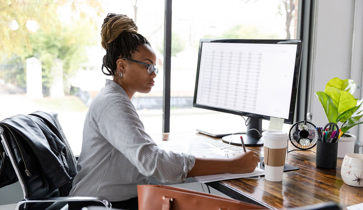 woman at desk, using computer with spreadsheet on monitor